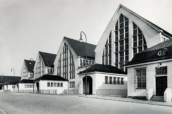 historische Schwarz-Weiß-Aufnahme der Großmarkthalle München. 4 spitze Giebel von hohen Hallen mit vielen kleinen Fenstern. Davon kleine Eingangsgebäude